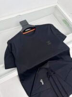 Maglietta nera minimalista con logo riflettente, su appendiabiti elegante, stile casual e sofisticato.