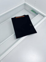 Maglietta nera minimalista con striscia arancione e logo discreto, display elegante su sfondo bianco.