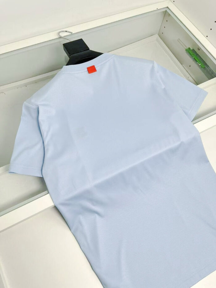 Maglietta blu pastello con dettaglio arancione, elegante e moderna, ideale per look casual e raffinati.