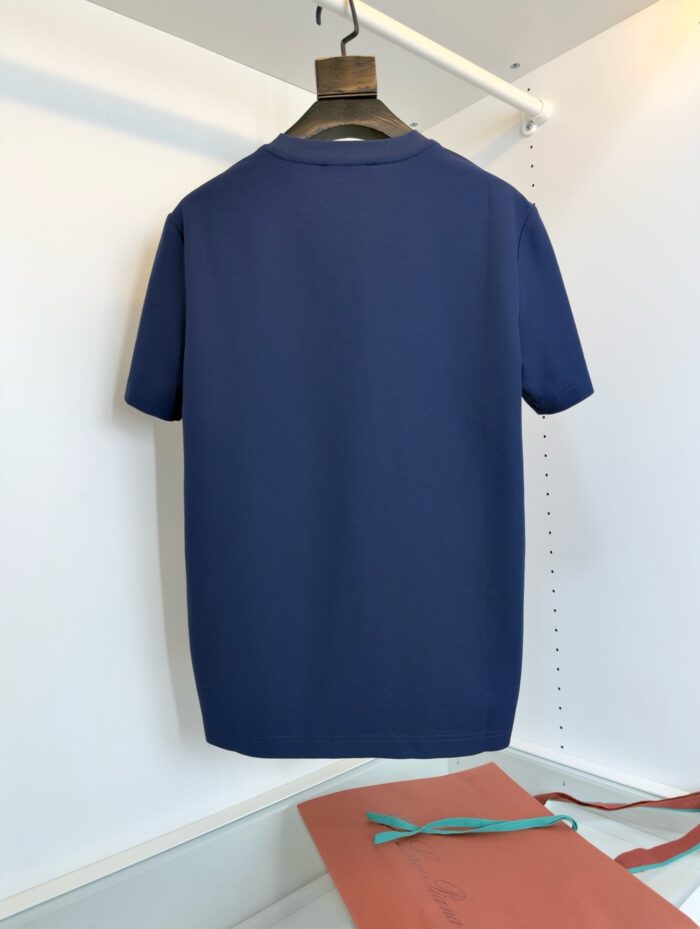 Maglietta navy blue minimalista con dettaglio arancione e accessorio blu, su appendiabiti di legno.