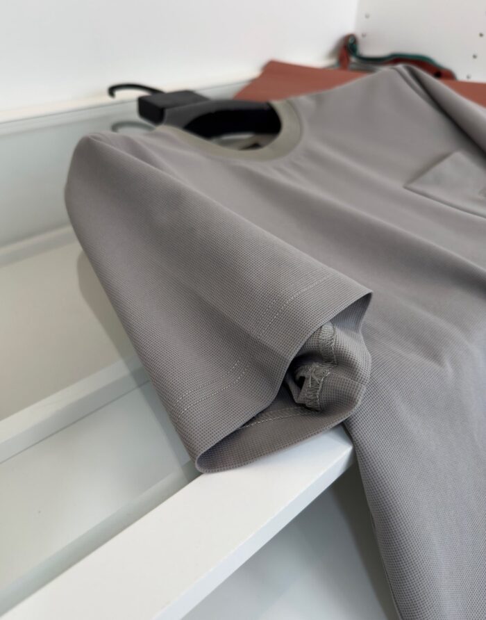 Maglietta grigia minimalista, piegata con cura su mensile, dallo stile casual e versatile.