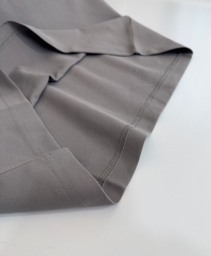 Tessuto grigio sottile e lucido con cuciture precise, ideale per abbigliamento elegante e versatile.