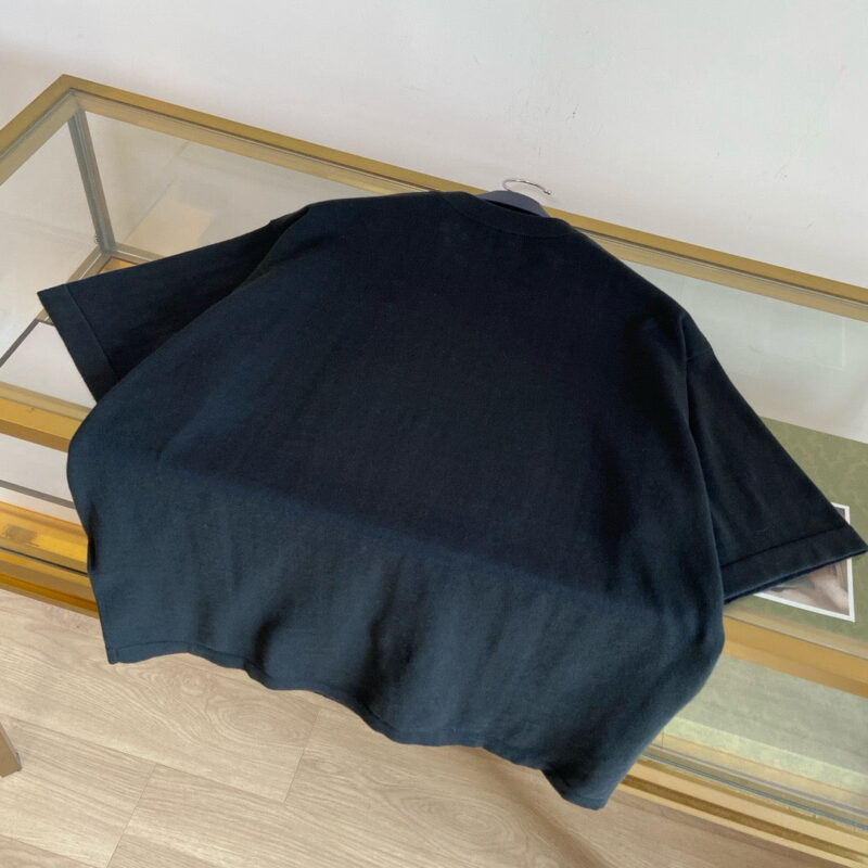 Maglietta nera minimalista su tavolo in vetro, stile elegante e contemporaneo.