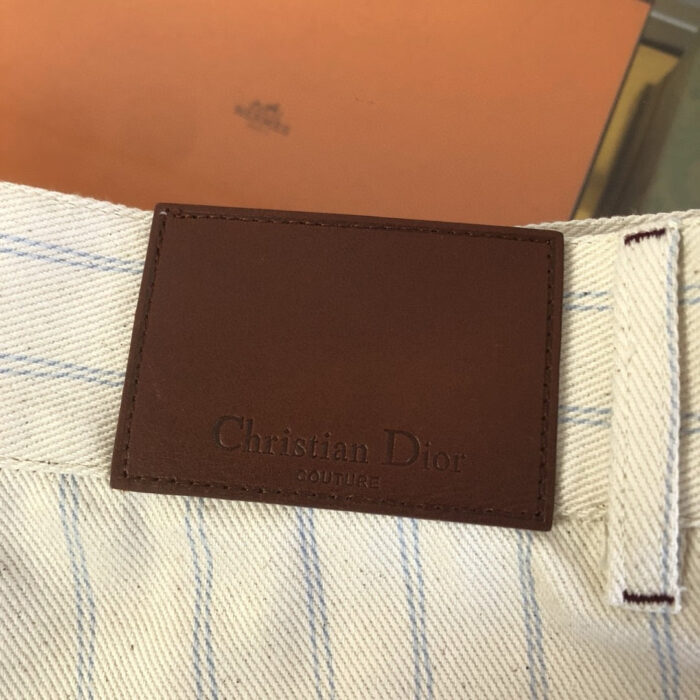 Dettaglio di jeans Dior con etichetta in pelle e strisce blu e bianche sul tessuto cotton