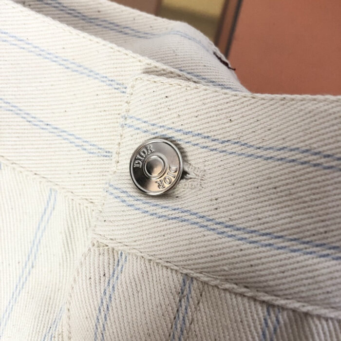 Bottoni Dior in metallo su pantaloni a righe casual e di lusso.