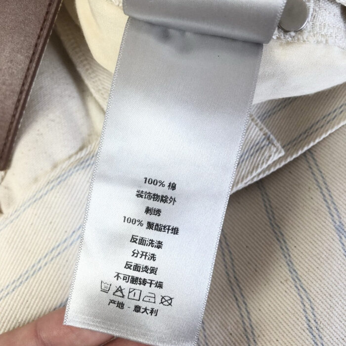 Etichetta di abbigliamento in cotone con istruzioni di cura e simboli internazionali.