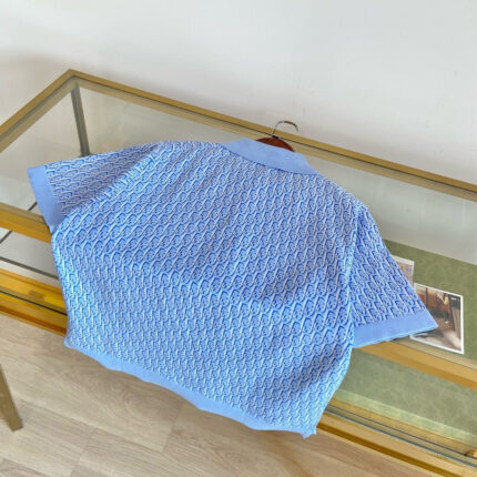 Camicia estiva blu con motivo ondulato, collo scuro, su tavolo di vetro elegante.