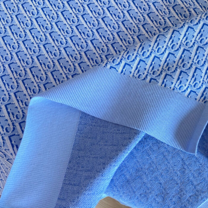 Tessuto blu con motivi intrecciati e bordo a costa, ideale per abbigliamento e arredo.