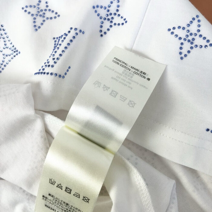T-shirt bianco con strass blu e dettagli a stella, care label visibile.