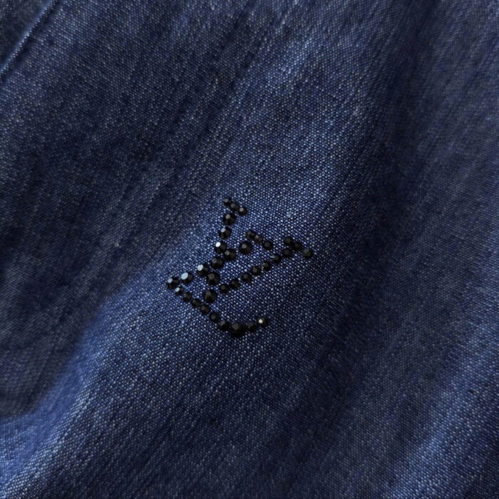 Dettaglio denim blu con logo ricamato nero, stile elegante e casual.