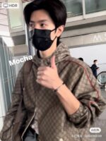 Giovane alla moda in aeroporto con mascherina, jacket di lusso e gesto di approvazione