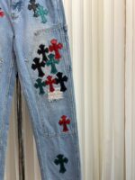 Jeans vintage con ricami di croci colorate e dettagli distressed, stile casual e artistico.