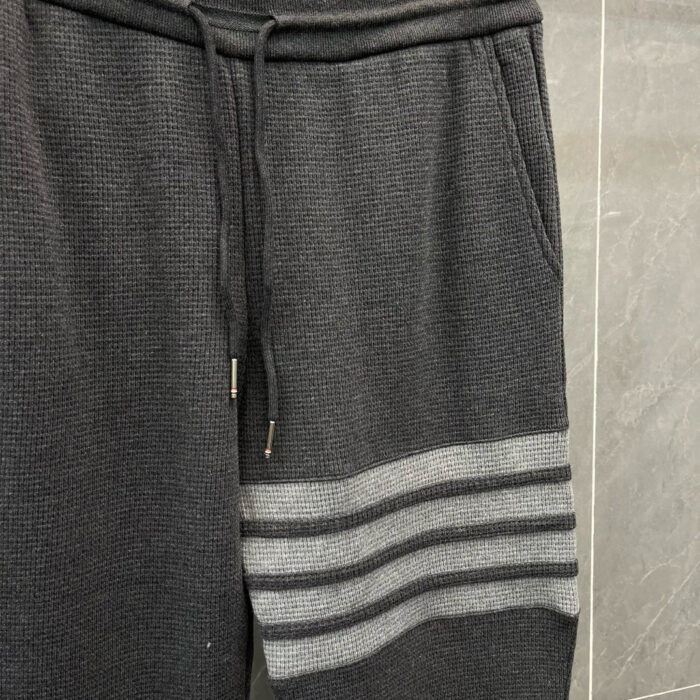Pantaloni sportivi neri con righe grigie a costina, elastico in vita e dettagli in metallo.