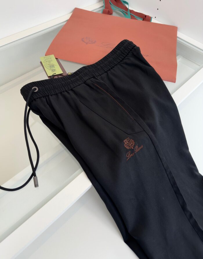 Pantaloni sportivi neri con logo rosso e borsa corallo, stile casual e athleisure elegante.