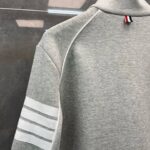 Felpa grigia sportiva con strisce nere, collo alto e dettaglio colorato sul colletto.