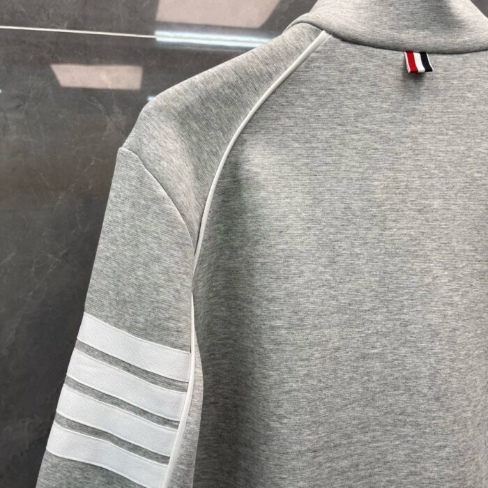 Felpa grigia sportiva con strisce nere, collo alto e dettaglio colorato sul colletto.