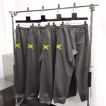 Pantaloni sportivi grigi con logo verde neon, stile casual e atletico, su appendiabiti moderno.