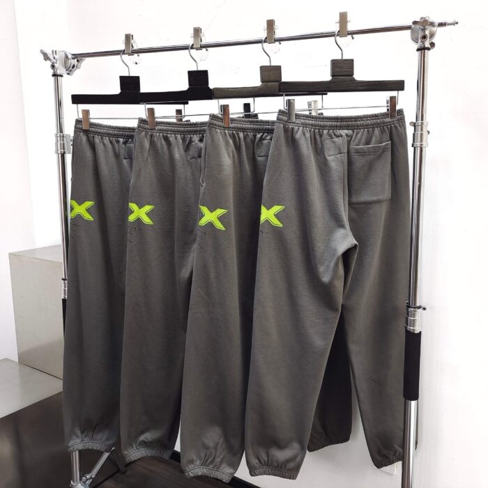 Pantaloni sportivi grigi con logo verde neon, stile casual e atletico, su appendiabiti moderno.