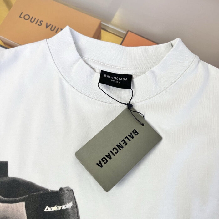 Maglietta bianca Balenciaga con etichetta di lusso, sfondo con scatole Louis Vuitton prestigiose.