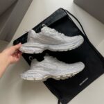Sneaker Balenciaga argentate e borsa di lusso moderna su sfondo bianco.