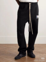 Pantaloni NBA neri con logo, cintura beige e sneakers sportive nere, stile casual e attivo.