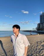 Ragazzo pensieroso sulla spiaggia di sera con vista mare e architettura moderna.