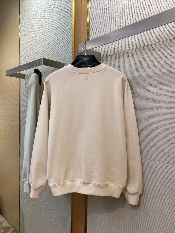 Maglione beige minimalista in cotone, stile casual ed elegante, in esposizione su hanger nello store.