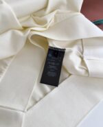 Etichetta cura su vestito crema in tessuto elegante, dettagli di manutenzione e materiali.