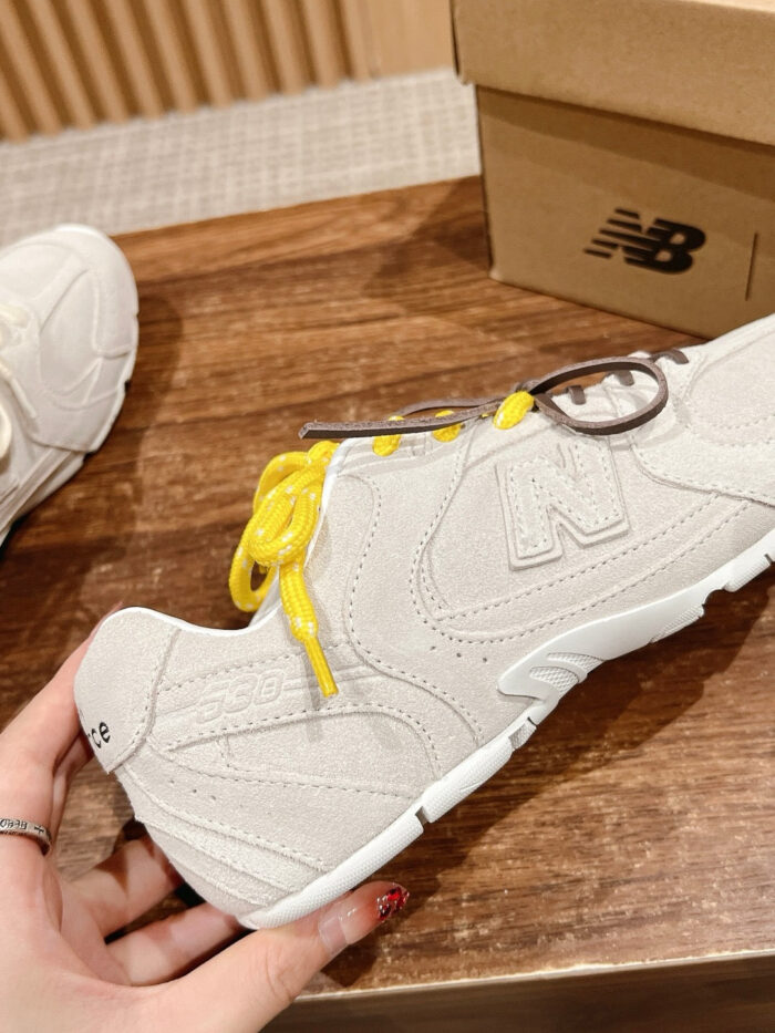 Sneaker beige New Balance con lacci gialli, stile casual e comfort su superficie in legno.
