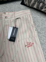 Pantaloni beige Dior con righe rosse, logo ricamato e dettagli di alta moda.