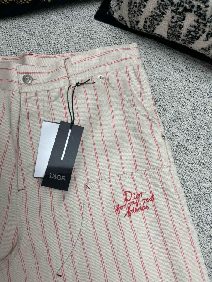 Pantaloni beige Dior con righe rosse, logo ricamato e dettagli di alta moda.