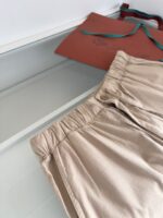 Pantaloni beige casual con borsa terracotta e dettagli verdi, stile minimalista ed elegante.