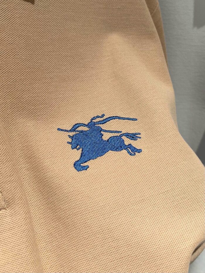 Maglietta polo beige con logo ricamato di cavallo in blu, stile classico e versatile.
