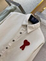 Camicia beige con patch a cuore rosso, stile casual-elegante, tessuto morbido in cotone, dettagli raffinati.