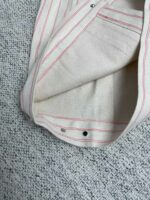 Dettaglio di camicia beige con strisce rosse e bottoni in metallo, moderna ed elegante.