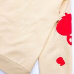 Felpa beige con accenti rossi e design giocoso, ideale per uno stile casual e originale.