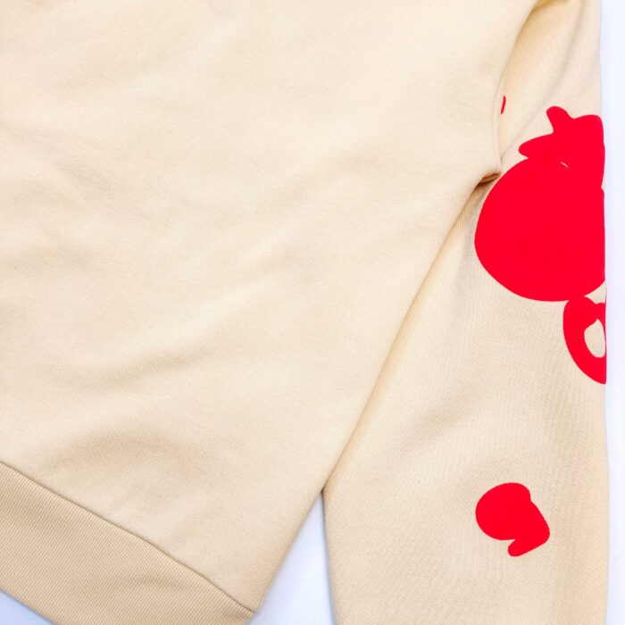 Felpa beige con accenti rossi e design giocoso, ideale per uno stile casual e originale.