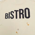 Maglietta casual con scritta BISTRO e macchie colorate, stile informale e originale.