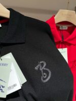 Magliette polo nere ed rosse eleganti con logo discreto e tag verde su appendiabiti.