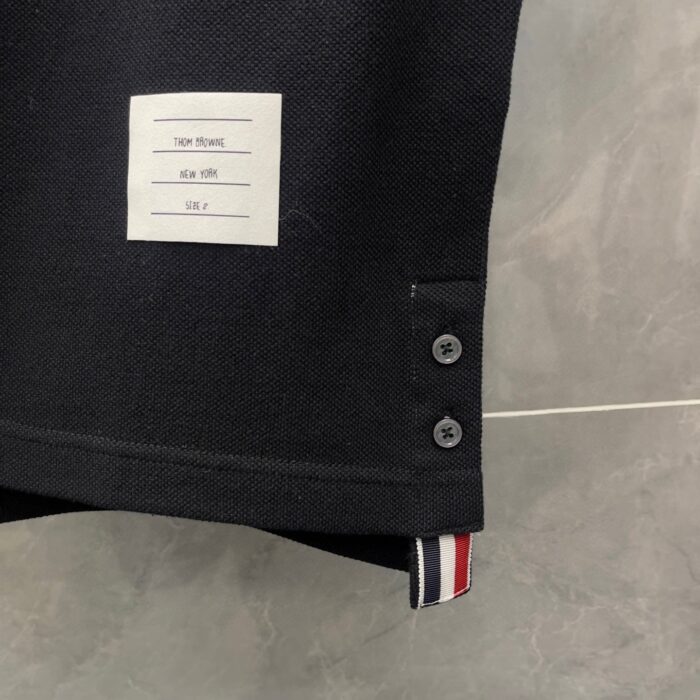 Polo nera casual con bottoni decorativi e dettaglio a strisce colorate sotto lorlo.