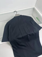Maglietta nera semplice su gruccia in ambiente minimalista, ideale per stile casual e versatile.