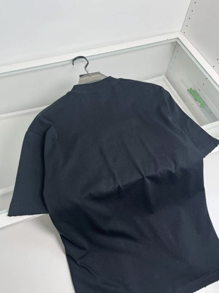 Maglietta nera semplice su gruccia in ambiente minimalista, ideale per stile casual e versatile.