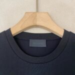 T-shirt nera a girocollo su appendiabiti di legno, stile minimalista e elegante.