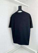 Maglietta nera semplice con scollo a giro, hanger e sfondo bianco.