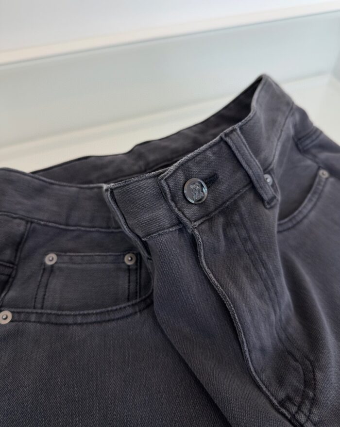 Pantaloni in denim grigio vintage con cintura, bottoni metallici e cuciture robuste.