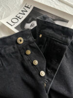 Jeans in denim nero con dettagli metallici sopra magazine di lusso LOEWE.