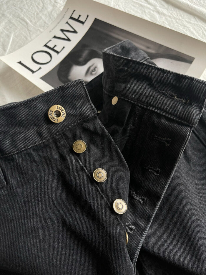 Jeans in denim nero con dettagli metallici sopra magazine di lusso LOEWE.