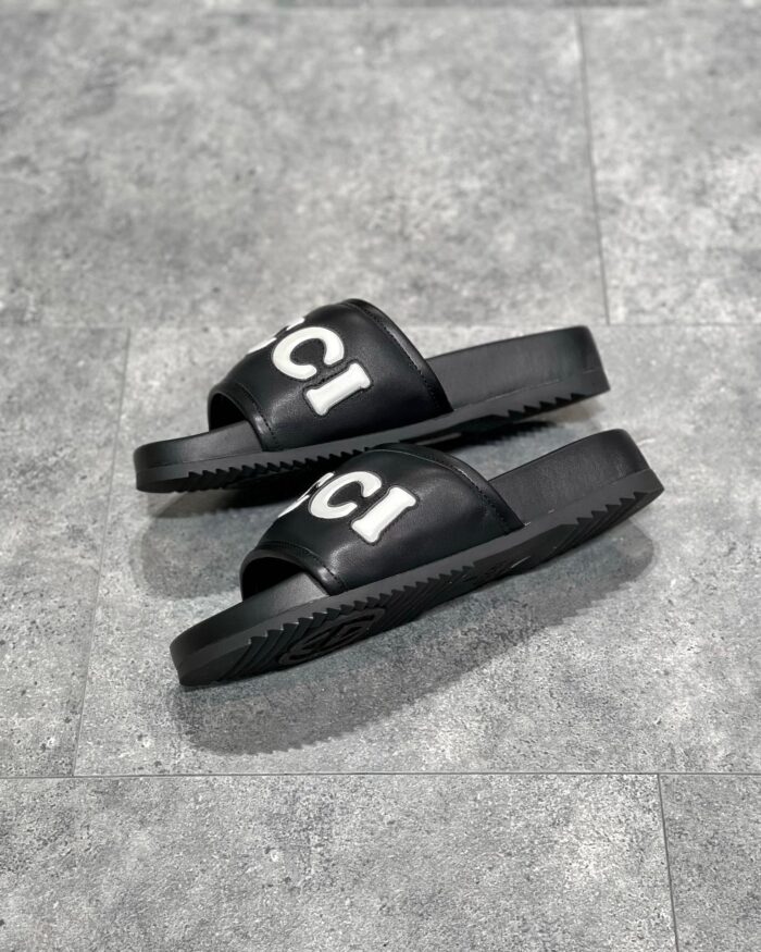 Sandali slip-on neri con logo bianco, suola antiscivolo, stile moderno e casual.