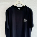 Maglietta nera elegante con logo ricamato, casual e versatile, su appendiabiti in ambiente minimalista.