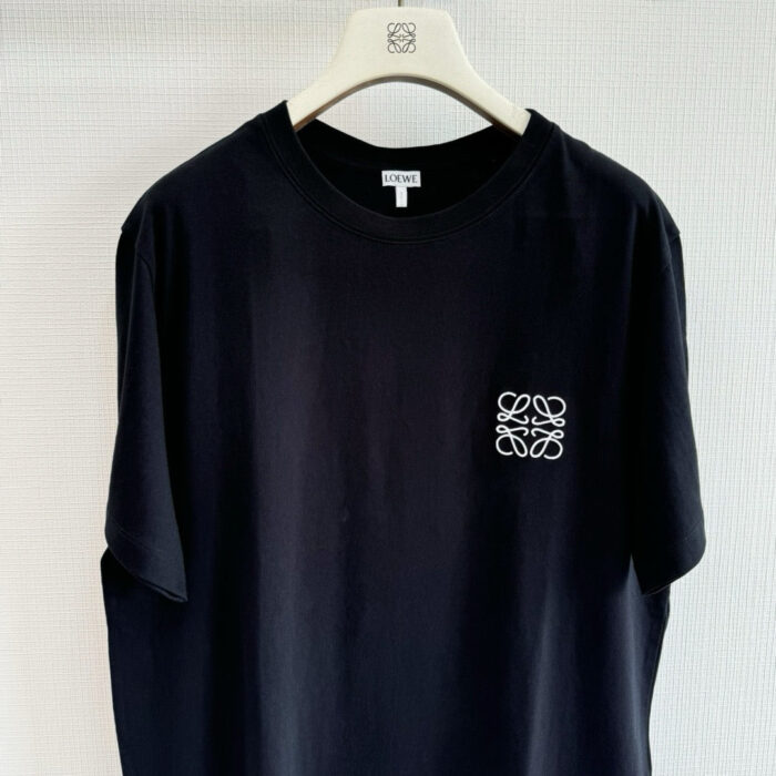Maglietta nera elegante con logo ricamato, casual e versatile, su appendiabiti in ambiente minimalista.